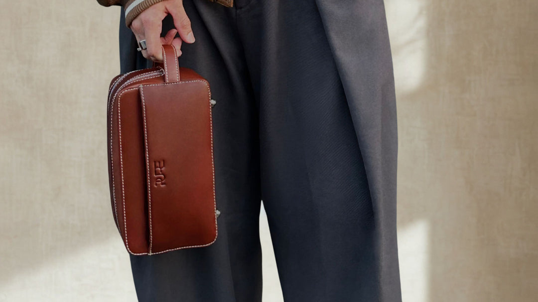 Braune minimalistische Lederhandtasche wird von einer Person an der Seite gehalten, modernes elegantes Design mit sichtbaren Ziernähten