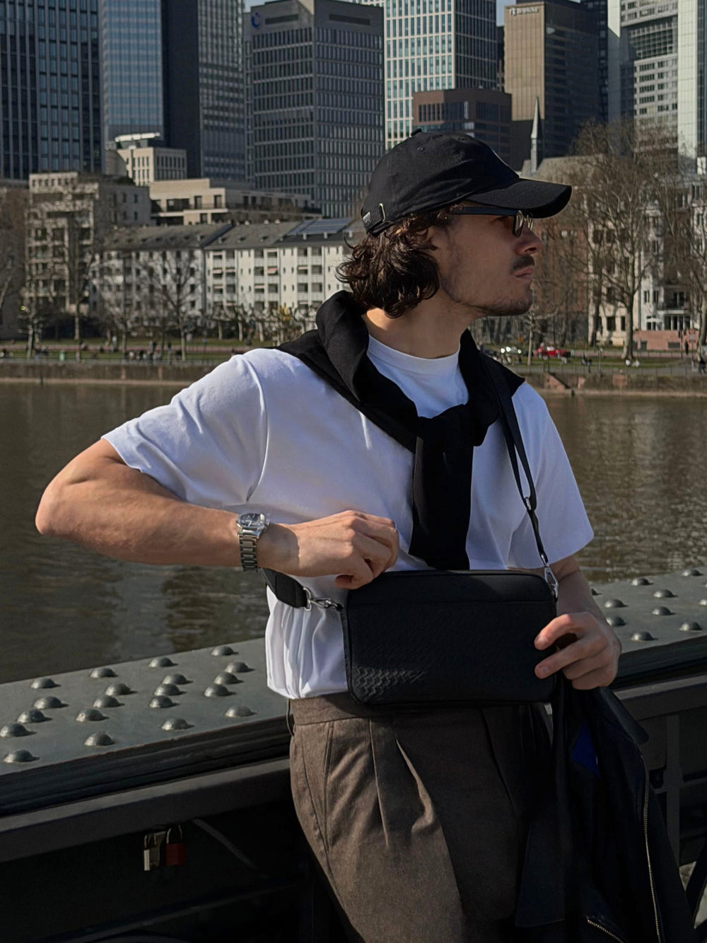 Geflochtene Umhängetasche Juno in Schwarz aus Leder, moderne Herren Crossbody Bag getragen von Model in urbaner Umgebung