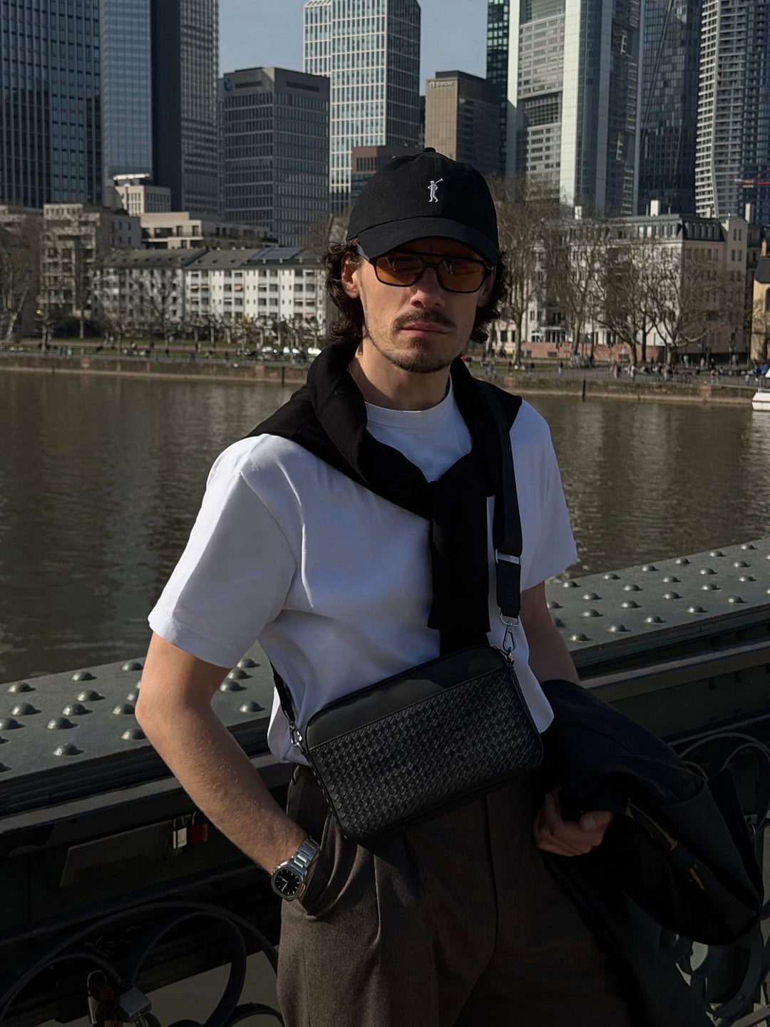 Schwarze geflochtene Crossbody Bag Juno aus Leder für Herren, stilvoll getragen von Model in der Stadt