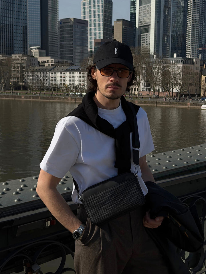 Schwarze geflochtene Crossbody Bag Juno aus Leder für Herren, stilvoll getragen von Model in der Stadt